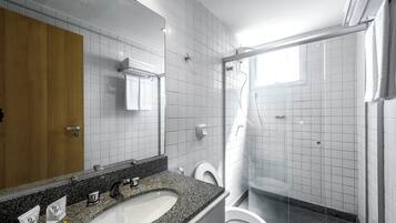 A modern bathroom with a granite countertop sink, a white toilet, and a glass-enclosed shower.