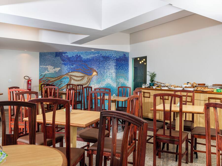 En restaurant med træborde og stole, en mosaikvæg og et køkkenområde med forskellige madvarer.