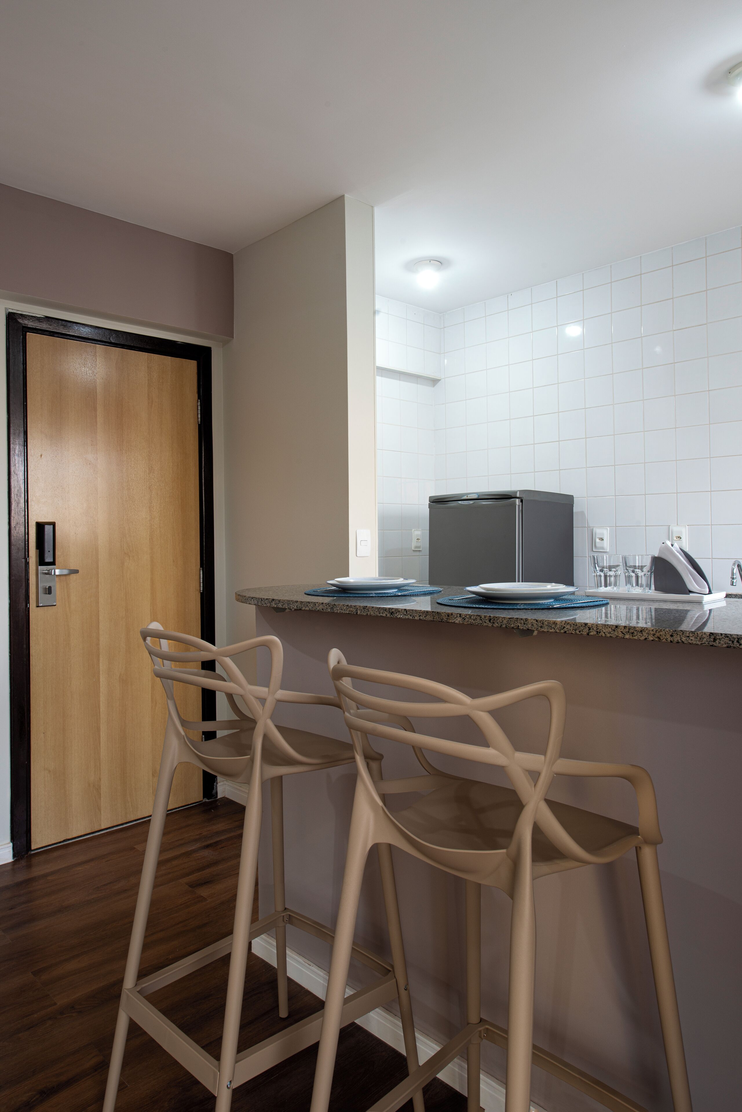 Una cocina con microondas, dos taburetes, una encimera y una puerta.