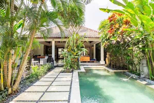 Relax by the tranquil pool surrounded by lush tropical plants and a covered seating area.