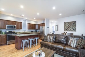 A modern kitchen with stainless steel appliances, a central island with stools, and a brown leather sofa in a living area with a large decorative wall piece. - ENTIRE BUILDING-Walk to Lincoln Park or The Beach! (Chicago)