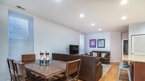 Una sala moderna con una mesa de comedor de madera, un sofá marrón oscuro y un televisor.