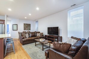 A modern living room with a brown leather sofa, a coffee table, a TV, and a large window with blinds. - ENTIRE BUILDING-Walk to Lincoln Park or The Beach! (Chicago)