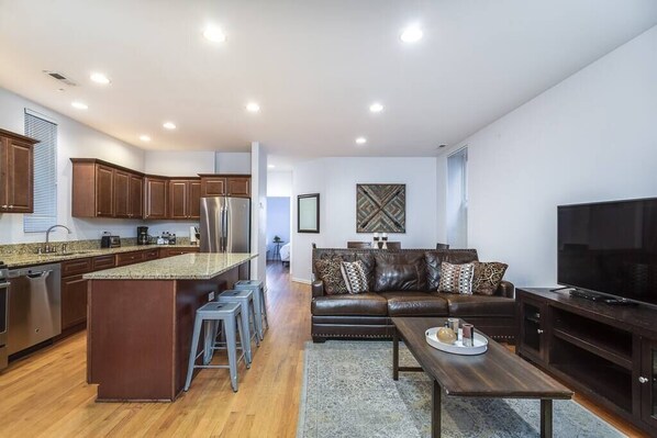 A modern kitchen with a central island, bar stools, a dark leather sofa, and a flat-screen TV. - ENTIRE BUILDING-Walk to Lincoln Park or The Beach! (Chicago)