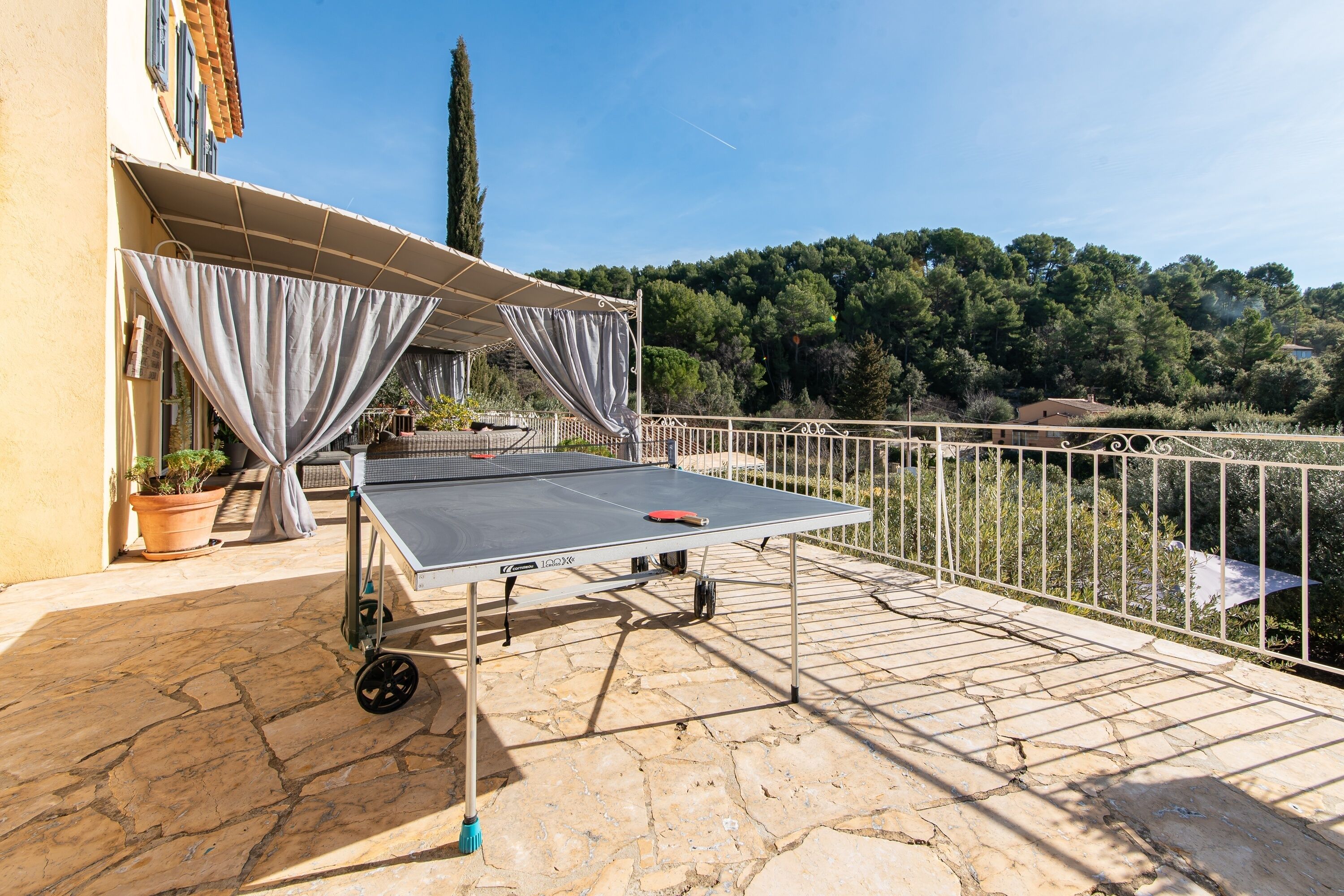 Una mesa de ping pong en un patio de piedra con vista a una colina boscosa.