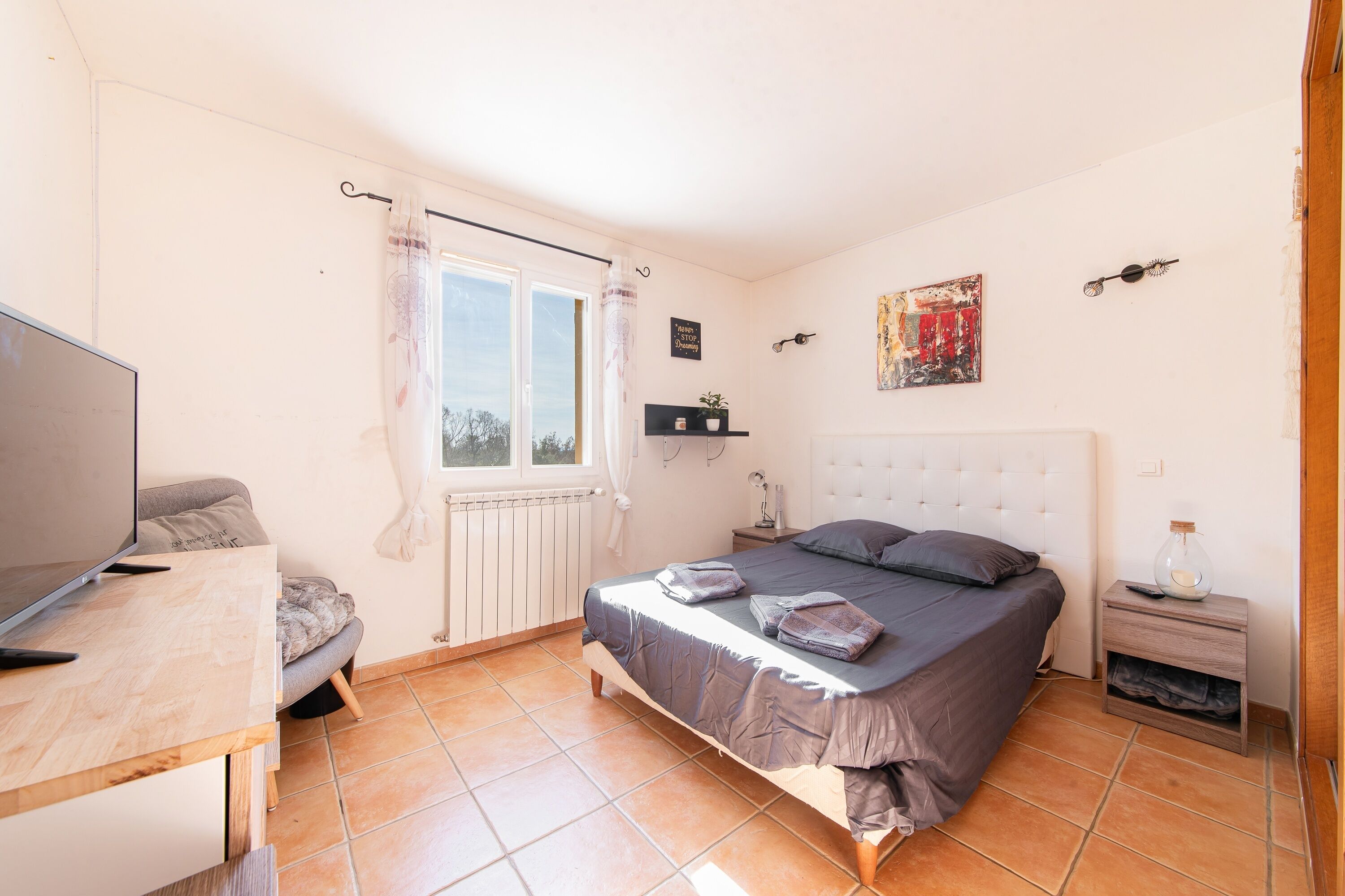 Ein Schlafzimmer mit einem Bett, einem Fernseher, einem kleinen Tisch und einem Fenster mit Vorhängen.