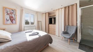 Un dormitorio con cama, una silla, una ventana y una pequeña cocina.