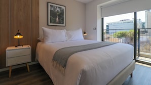 Een moderne hotelkamer met een groot bed, een nachtkastje met een lamp, een ingelijst beeld aan de muur en een balkon met uitzicht op de stad.