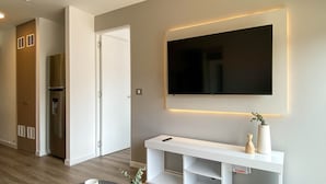 Een moderne woonkamer met een flatscreen televisie aan de wand, een witte console tafel en een ronde houten salontafel met een vaas.