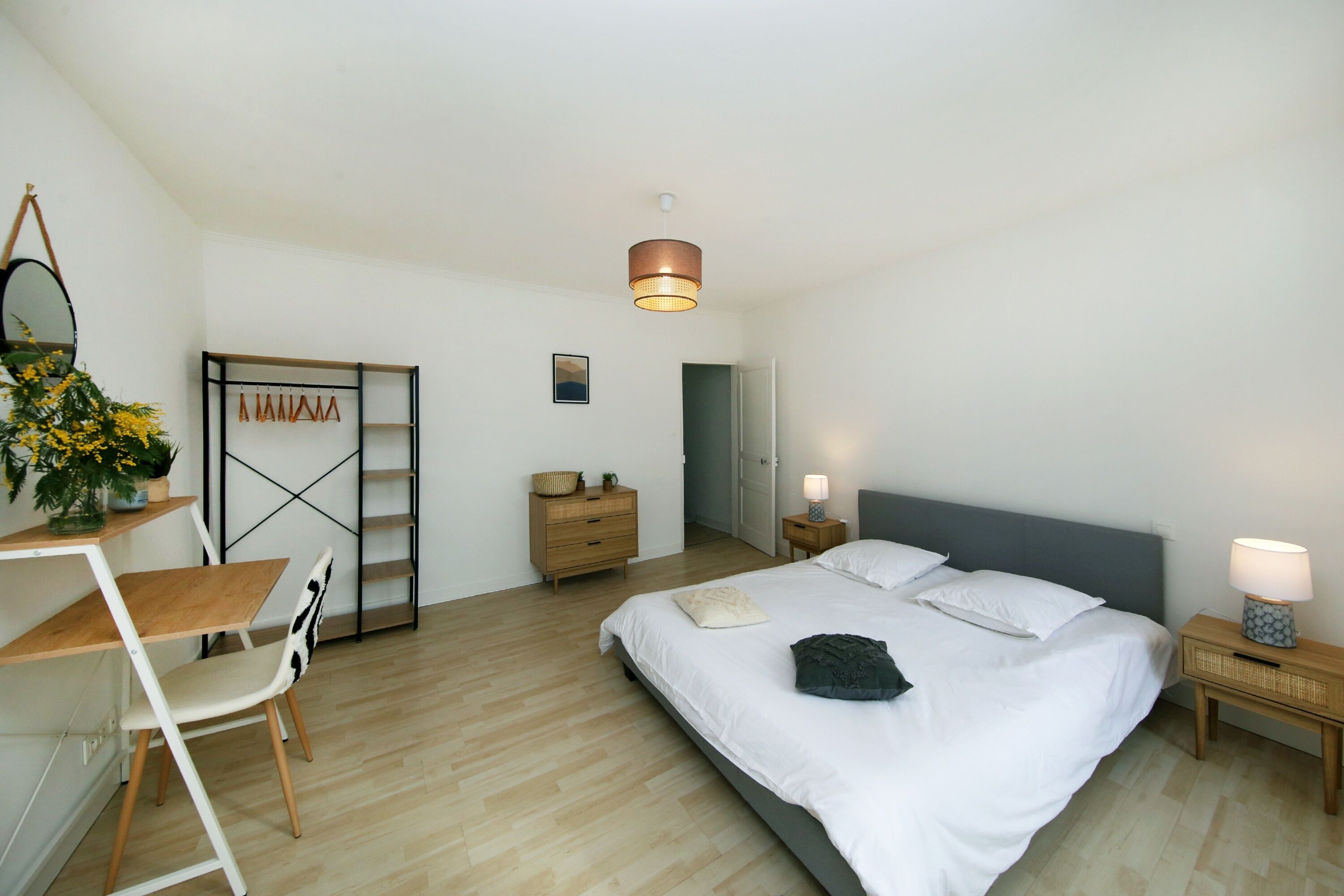 A bedroom with a bed, bedside tables, a desk, a chair, a wardrobe, and a hanging light fixture.
