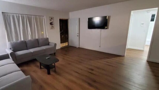 Een woonkamer met een grijze bank, een zwarte salontafel en een flatscreen televisie aan de muur.