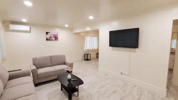A spacious living room with a beige sofa, a black coffee table, and a flat-screen TV mounted on the wall. - 2 bedroom 1 bathroom, Cozy home (South El Monte)
