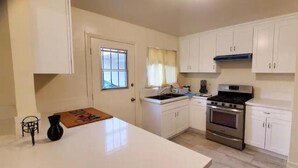 A compact kitchen with white cabinets, a stove, and a sink. - 2 bedroom 1 bathroom, Cozy home (South El Monte)