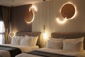Una habitación de hotel con dos camas, una lámpara de pared circular grande y una ventana con cortinas.