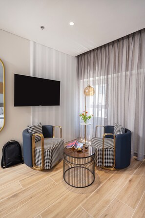 A modern living room with a flat-screen TV, two armchairs, a round coffee table, and a floor lamp. - Allenbeach TLV- Apt Hotel-Adults only (Tel Aviv)