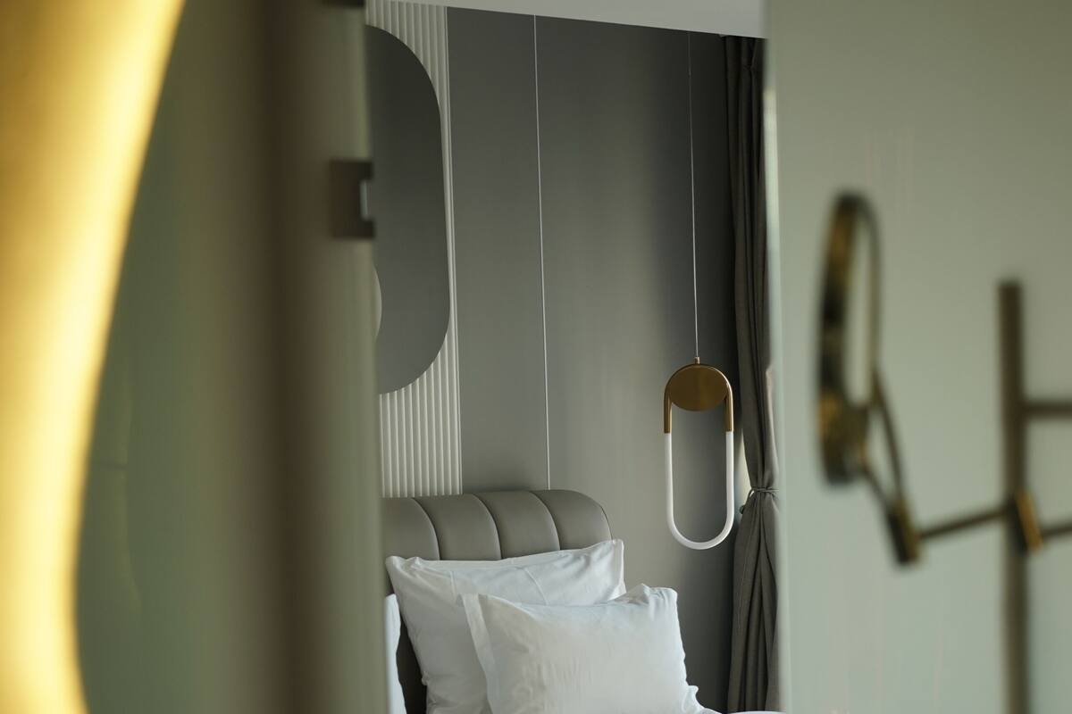 A modern hotel room with a bed, a hanging light fixture, and a view of the room through a glass door.