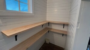 Une pièce d’angle avec des murs recouverts de panneaux blancs, une fenêtre et trois étagères en bois.