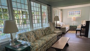 Un salon avec un canapé à motifs floraux, deux fauteuils, une table basse et un piano.