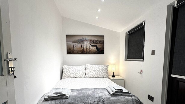 Ein modernes Schlafzimmer mit einem großen Bett, einem Bild an der Wand und einem Fenster mit Jalousien.