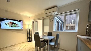 Ein Essbereich mit Tisch und Stühlen, einem Fernseher an der Wand und einem Fenster mit Blick auf ein Gebäude.