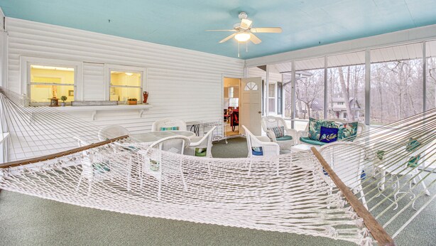 A hammock lounge with white wicker furniture, a ceiling fan, and large windows offering a view of the outdoors. - Central & Ornate Sewanee Home w/ Screened-In Porch (Sewanee)