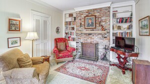 A living room with a fireplace, bookshelves, a red armchair, and a television. - Central & Ornate Sewanee Home w/ Screened-In Porch (Sewanee)