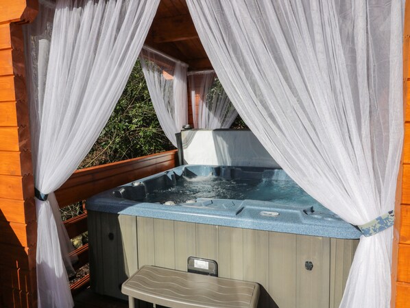 A hot tub with a wooden deck and a small table in front, surrounded by white curtains.