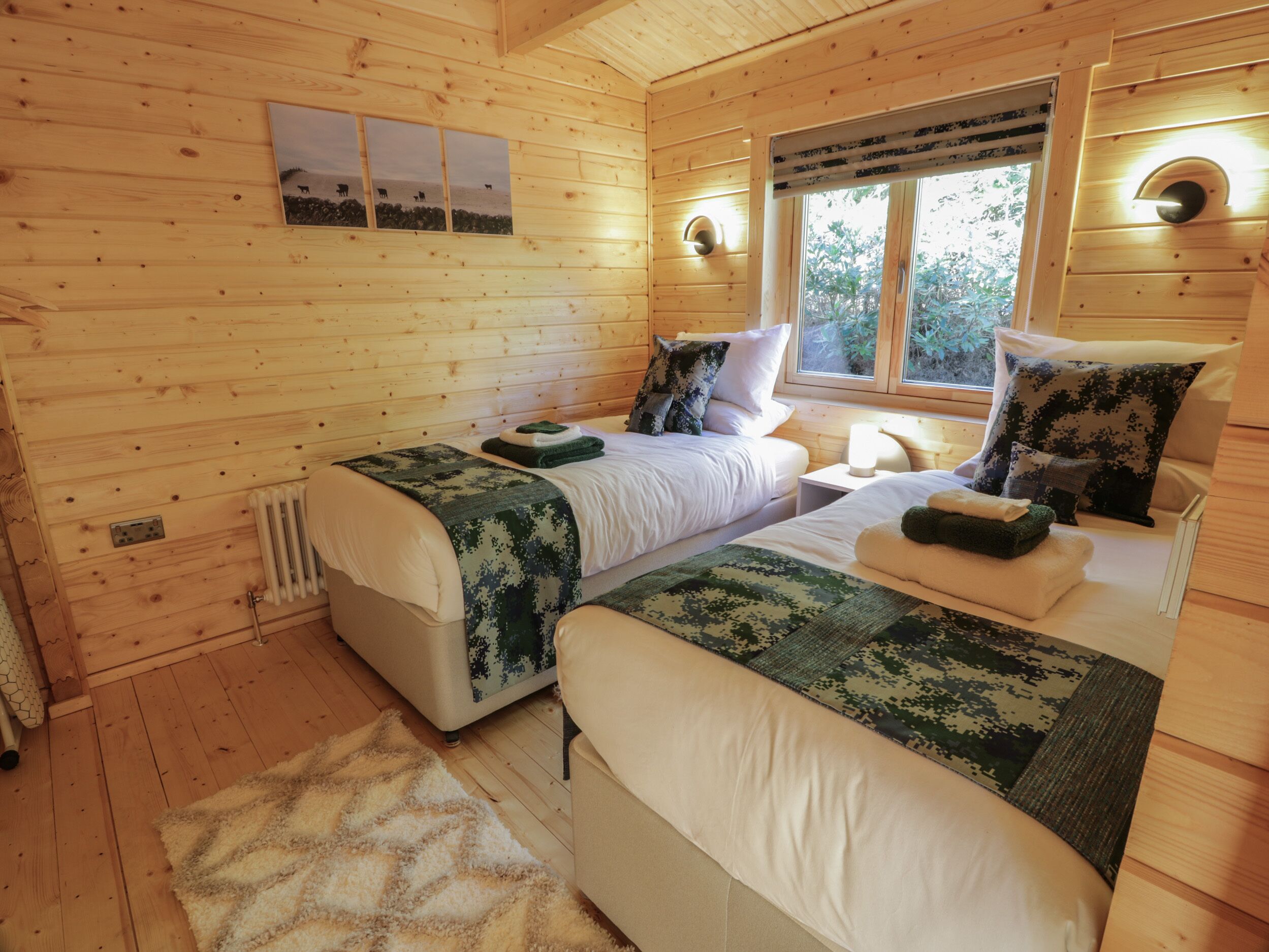 A wooden cabin bedroom with two beds, a window, and a wall-mounted light fixture.