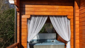 A wooden cabin with a hot tub, a table, and a bench. - Little Lodge (Newton Stewart)