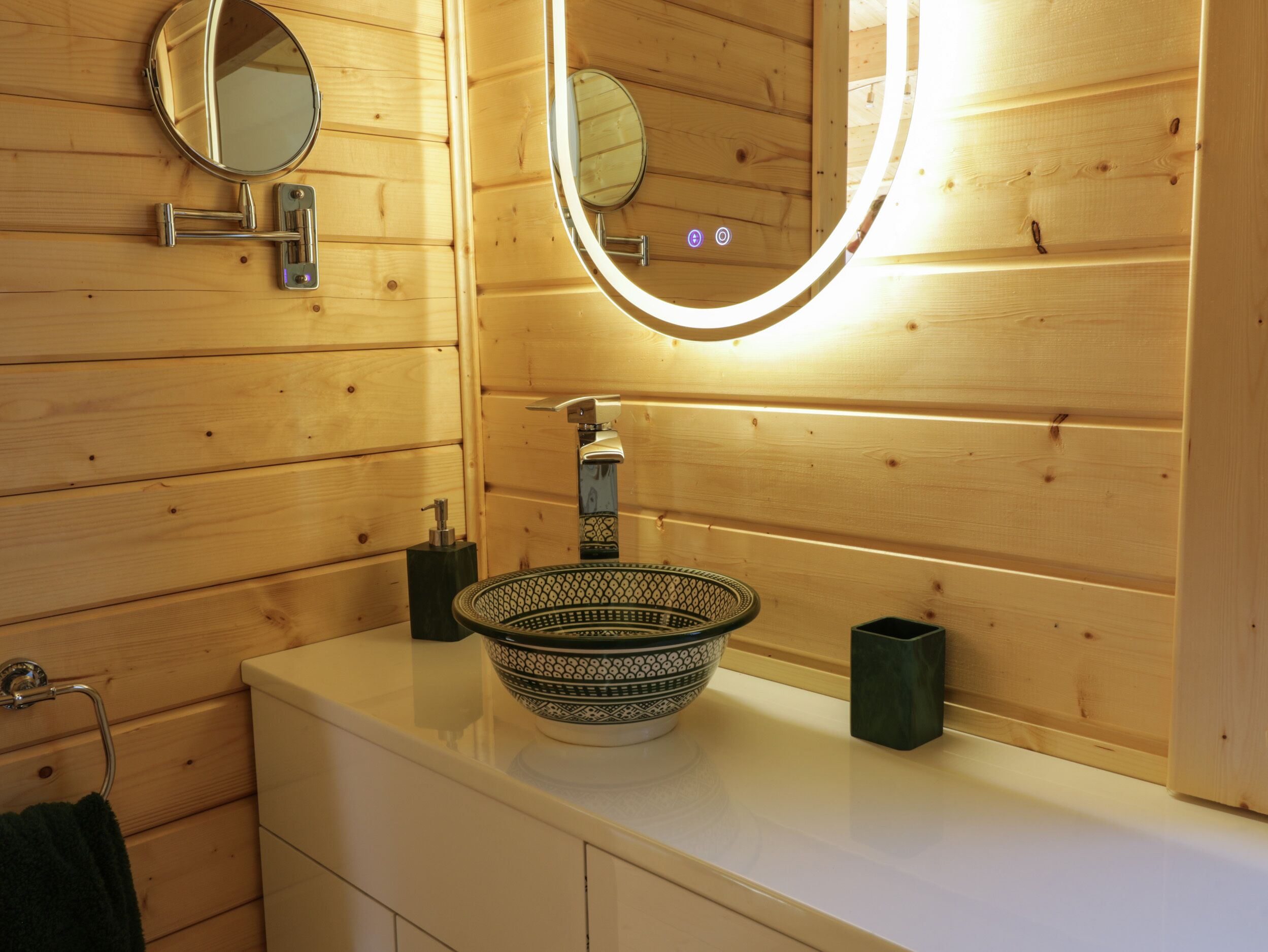 A wooden cabin bathroom with a round mirror, a sink with a decorative bowl, and a towel rack.