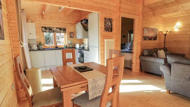 A cozy wooden cabin interior with a dining area, kitchen, and living room. - Little Lodge (Newton Stewart)