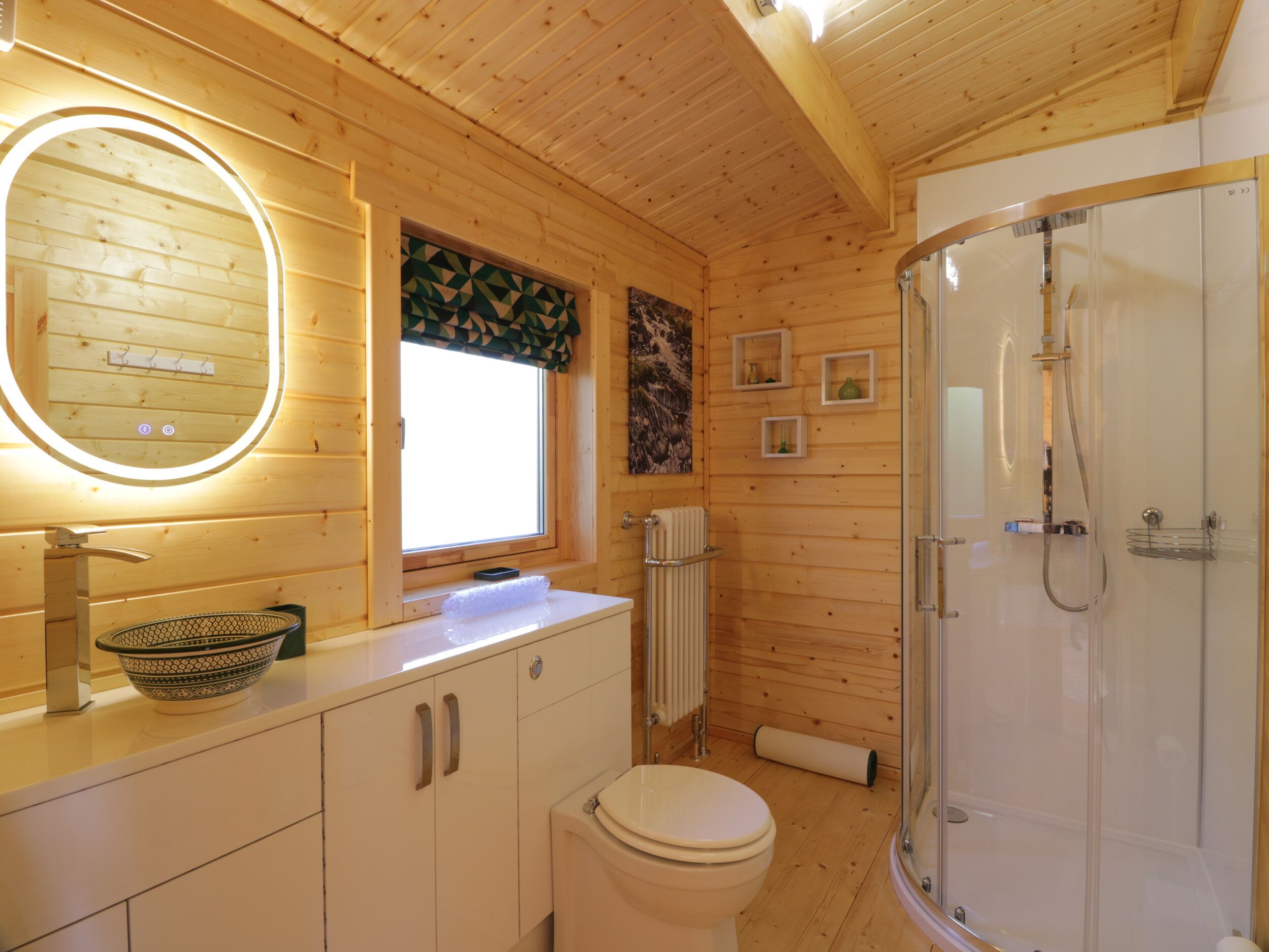 A wooden cabin bathroom with a toilet, sink, and shower.