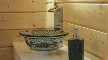 Une salle de bain avec un mur en bois, un comptoir blanc, un lavabo décoré de motifs verts et blancs, et un distributeur de savon noir.