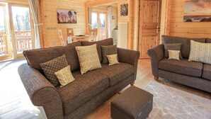 A cozy cabin interior with two sofas and a dining table, wooden walls, and a large window. - Little Lodge (Newton Stewart)