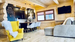 En modern inredning med en gul fåtölj, en grå soffa, trägolv, ett köksområde och ett stort fönster.