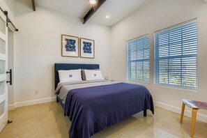 Un dormitorio con una cama, dos cuadros enmarcados, una ventana con persianas y una silla.