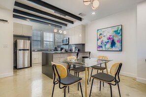 Una cocina moderna con un refrigerador de acero inoxidable, un microondas y un comedor con mesa y sillas de vidrio.