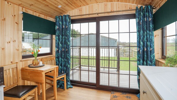 Een houten hut met een eethoek, een bank, een tafel met een bloevas en een uitzicht door een glazen deur.