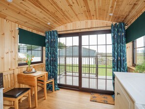 A wooden cabin with a dining area, a bench, a table with a vase of flowers, and a view through a glass door to the outside. - Tal Sarn Shepherd Hut (Llanfairpwllgwyngyll)