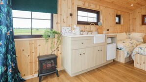 Een gezellig houten kamer in chaletstijl, met een groot raam, een klein fornuis, een gootsteen en een bed met bloemenbeddengoed.