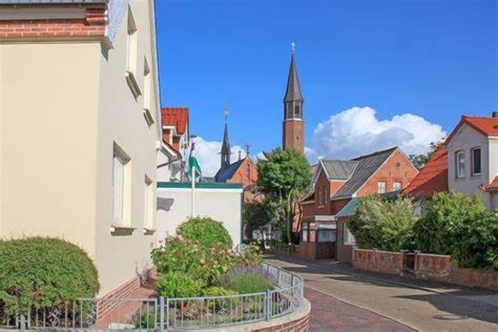 A street view with a church steeple, a building with a flag, and a paved road.