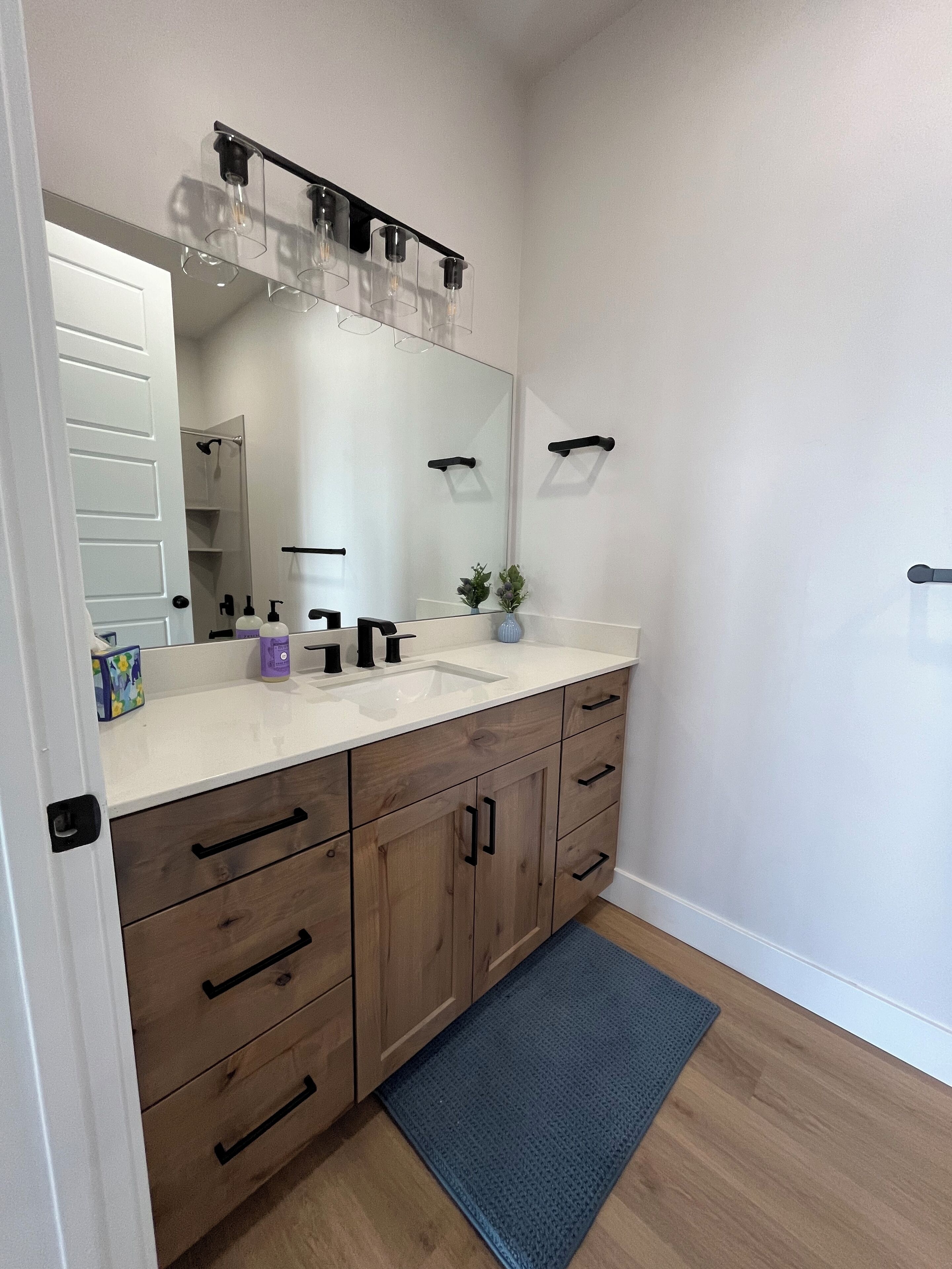 A bathroom with a white sink, wooden vanity, and a large mirror.