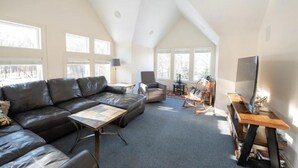 A spacious living room with a high ceiling, a leather sofa, a wooden coffee table, a TV stand, and a fireplace. - Peaceful Retreat (Minneapolis)