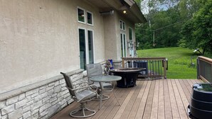 A wooden deck with outdoor furniture, a hot tub, and a view of a green lawn and trees. - Peaceful Retreat (Minneapolis)