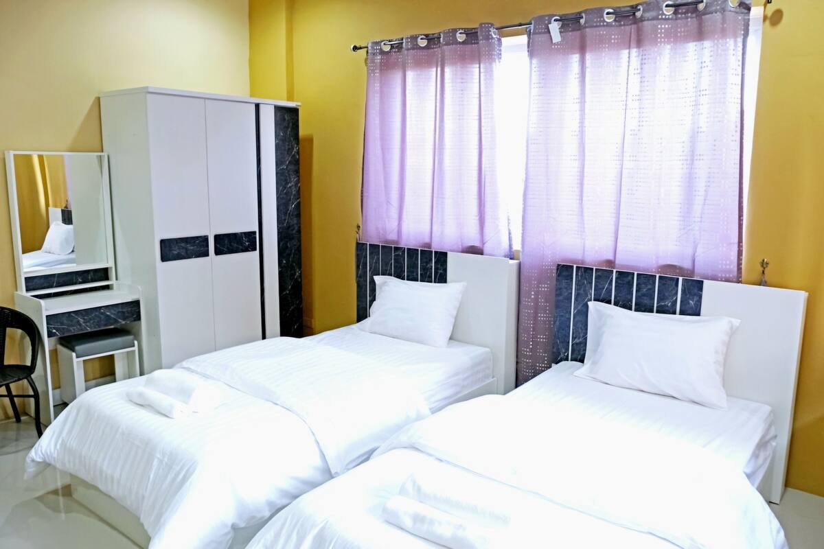 A hotel room with two beds, a wardrobe, a desk, and a chair.