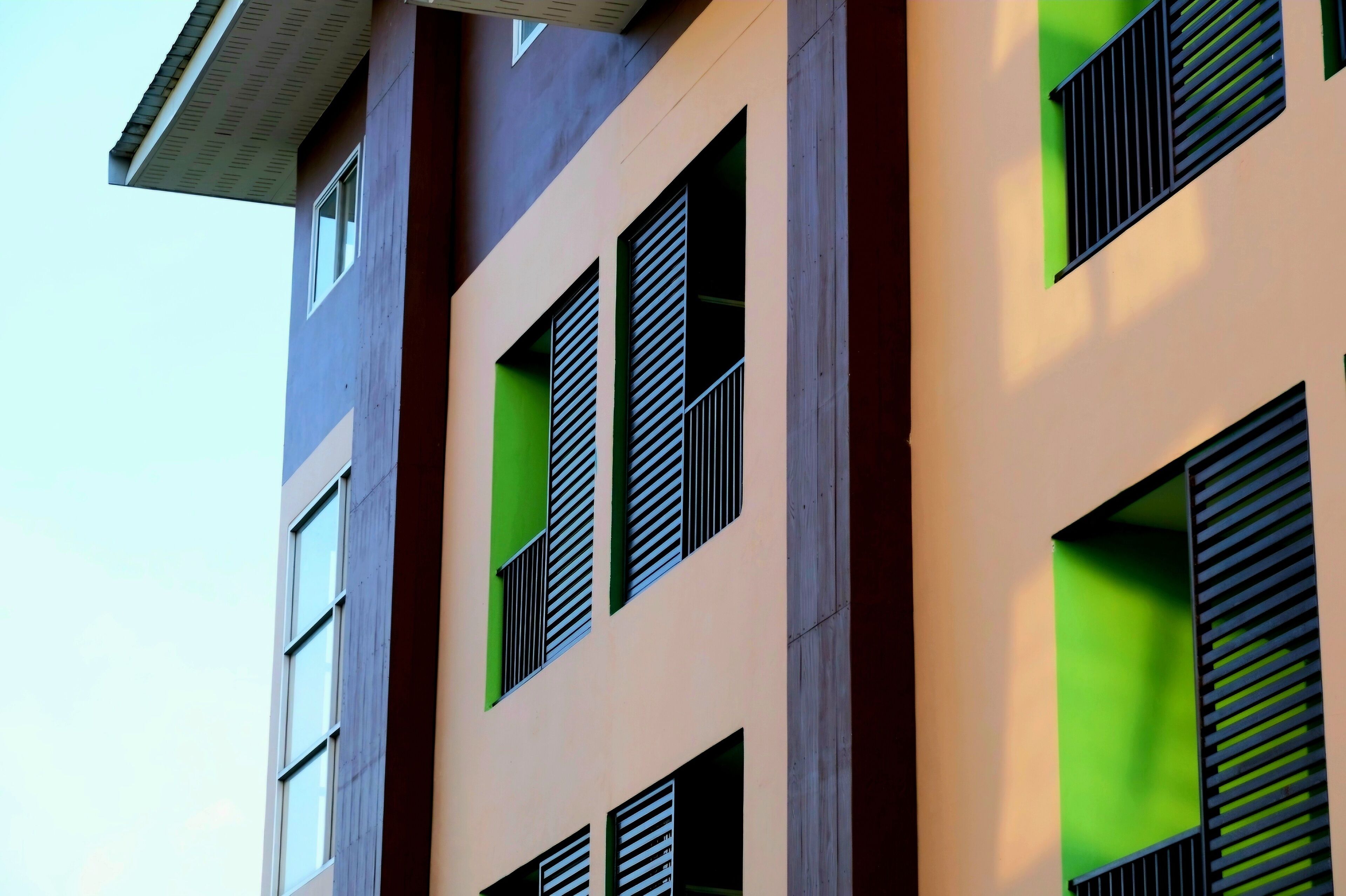 Un immeuble à plusieurs étages doté d’une architecture moderne, caractérisé par de grandes fenêtres équipées de stores horizontaux et un toit plat.
