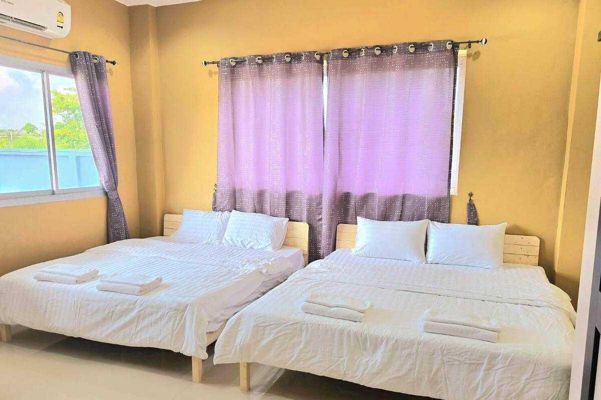 A hotel room with two beds, a window with curtains, and an air conditioning unit.