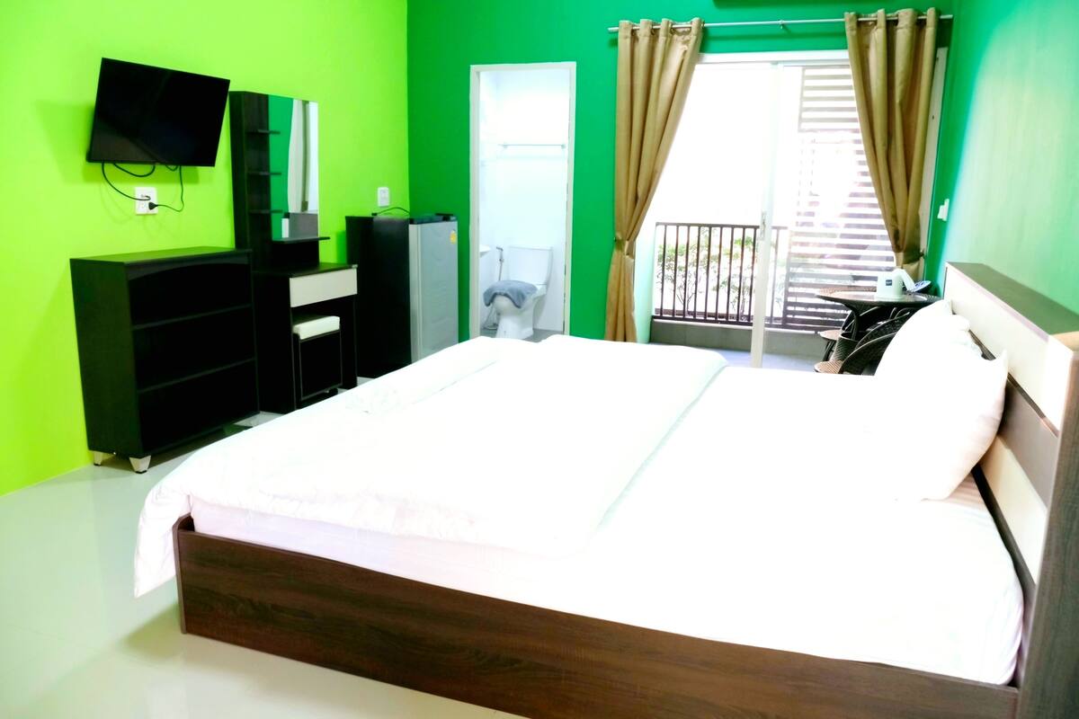 A hotel room with a bed, a TV mounted on the wall, a wardrobe, and a balcony with curtains.