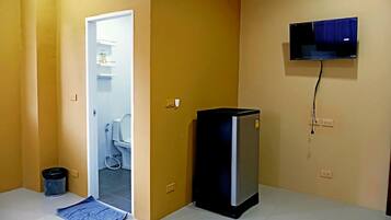 Una habitación pequeña con una puerta que da a un baño, un televisor montado en la pared y un refrigerador pequeño.