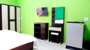 Une chambre comprenant un lit, un téléviseur fixé au mur, une armoire, un bureau avec une chaise et un réfrigérateur.